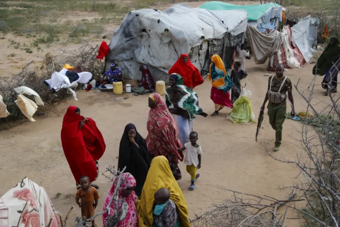 Somali refugees and an armed Kenyan policeman walk next to a makeshift shelter in Dadaab refugee camp in northern Kenya, Thursday, July 13, 2023. (AP Photo/Brian Inganga)