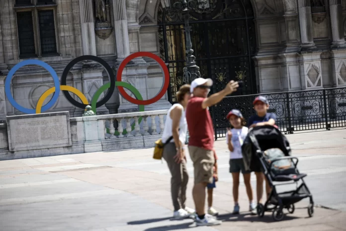 A family takes a selfie by the rings of the Olympic Games in front of the Paris townhall , Saturday, July 8, 2023 . The venue will host the start of the Olympic games’ s marathon in the Paris 2024 Olympics. (AP Photo/Thomas Padilla)