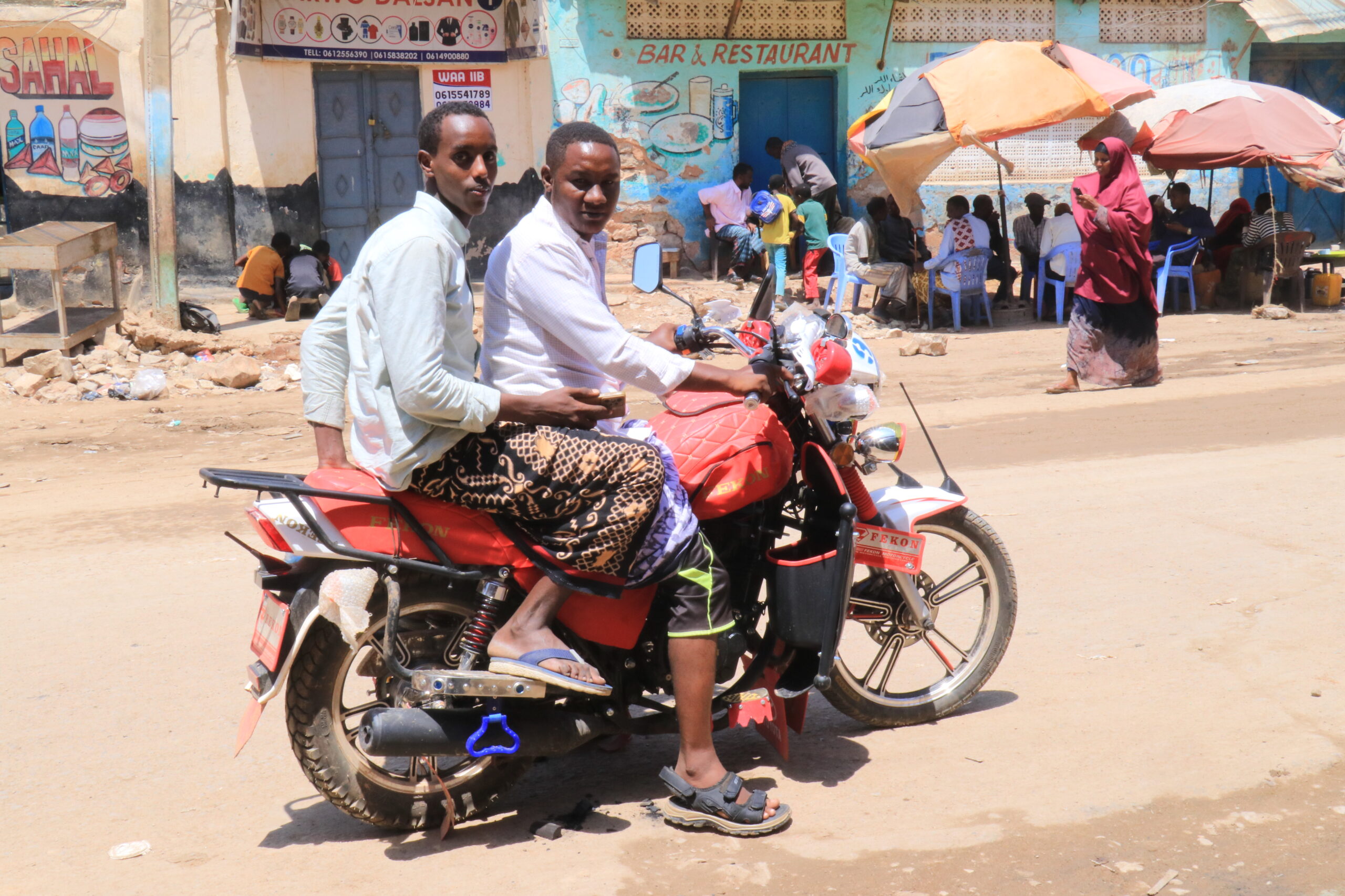 Young men ride a motorcycle as a woman passes the road through the streets of Baidoa, Somalia, in October. | PHOTO: Nurto Hussein.