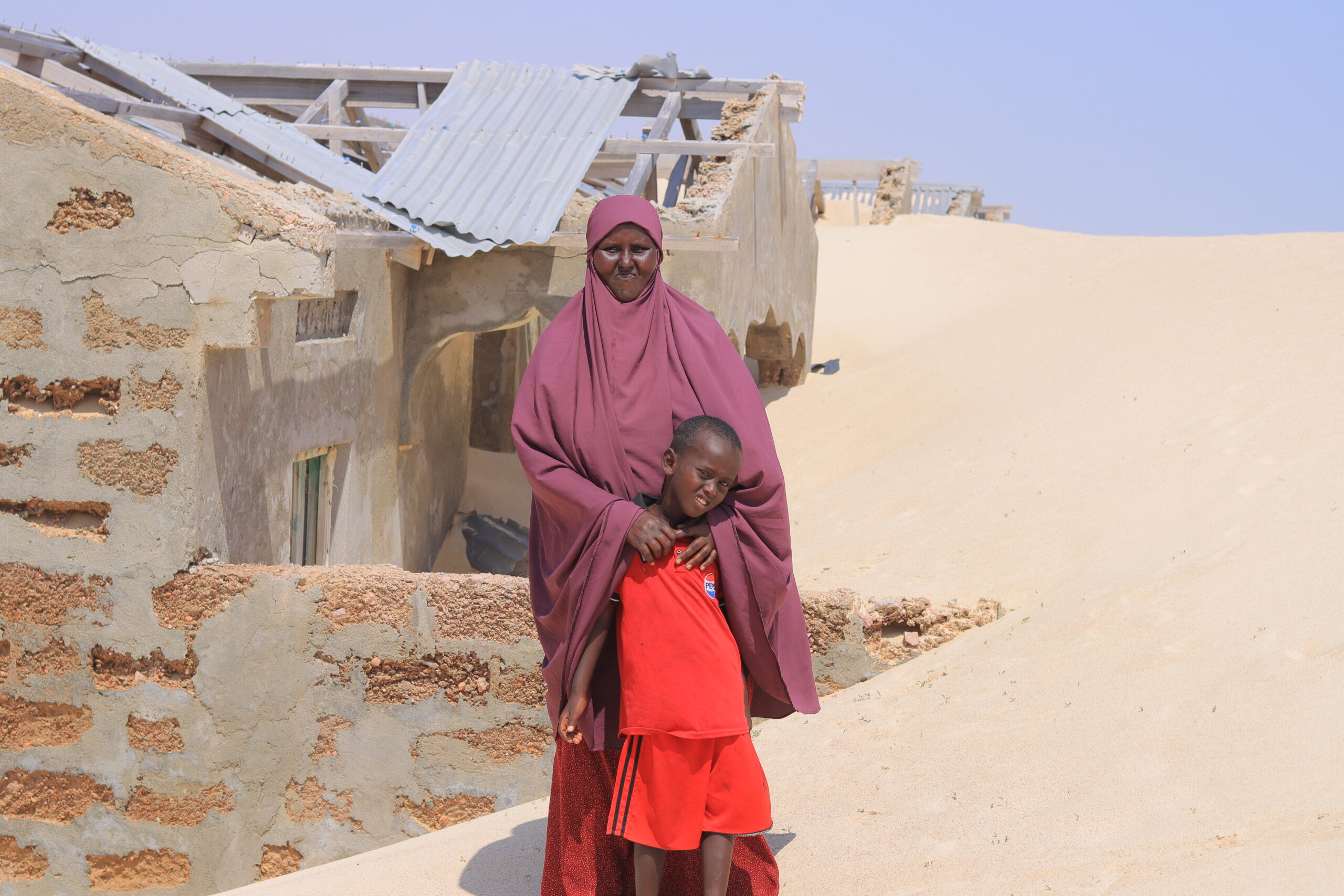 A woman stands near her house, which has been covered by sand due to the impacts of climate change, in Kulub village, eastern Mudug region, central Somalia. | PHOTO: Said Abdullahi.